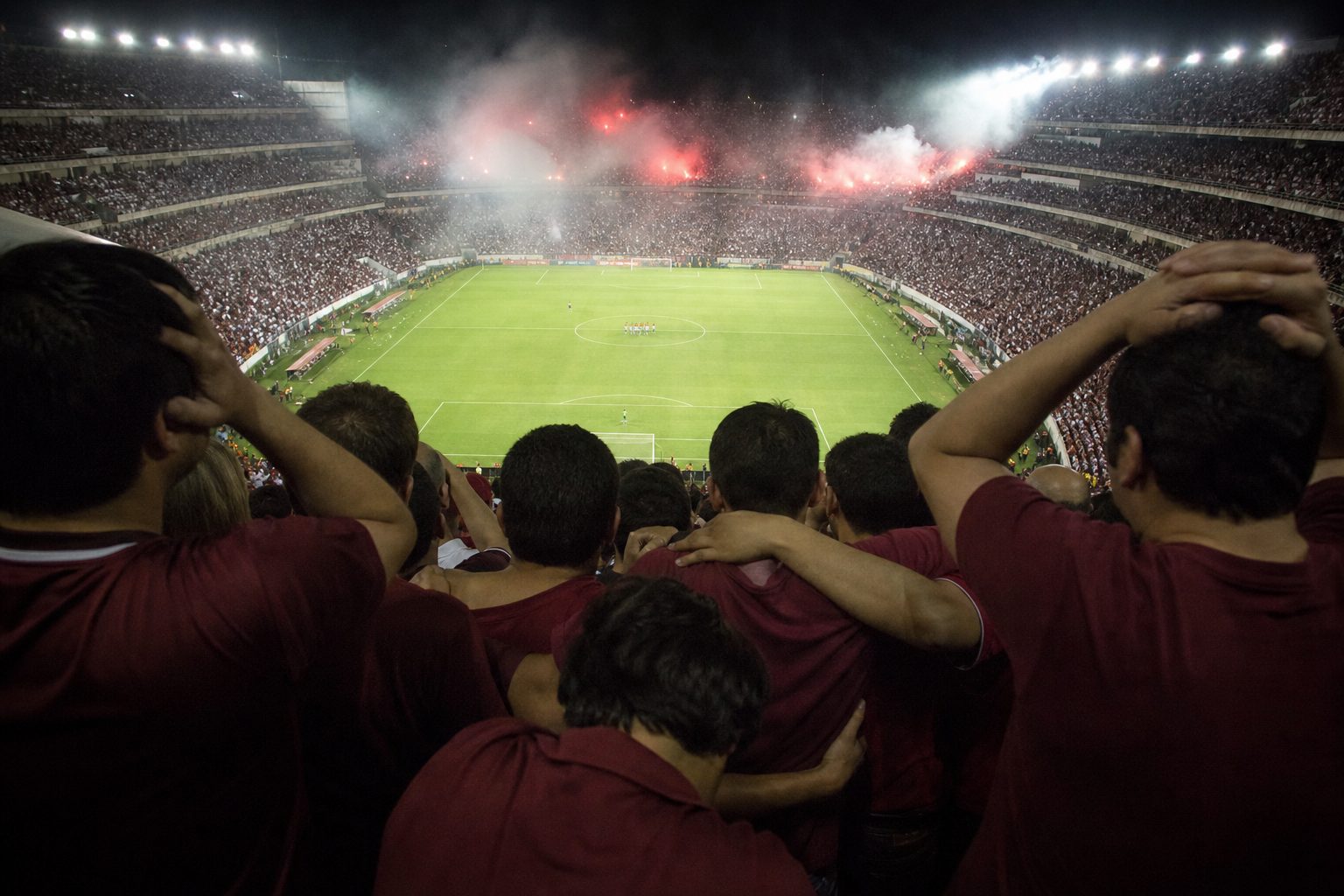 Anxious fans in burgundy shirts clutching each other during a night-time shoot-out (picture made with AI)