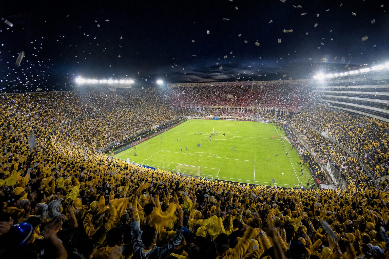 Fans in yellow and in red and white filling a South American stadium at night (picture made with AI)