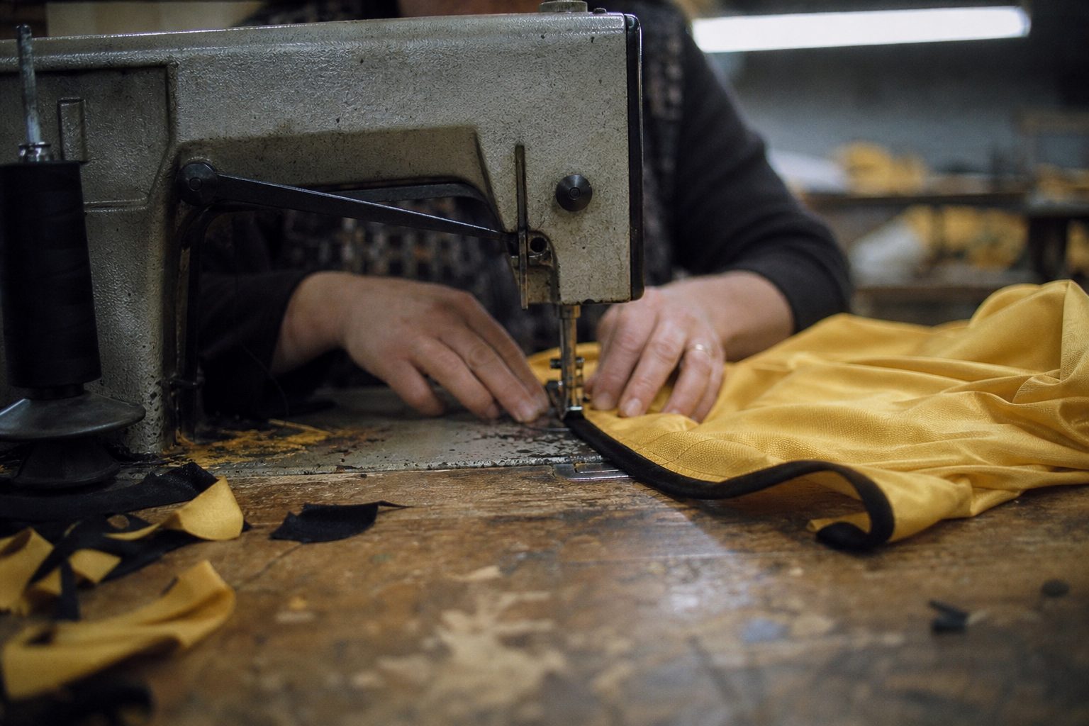 Sewing machine stitching the hem of a gold shirt in a small factory (picture made with AI)