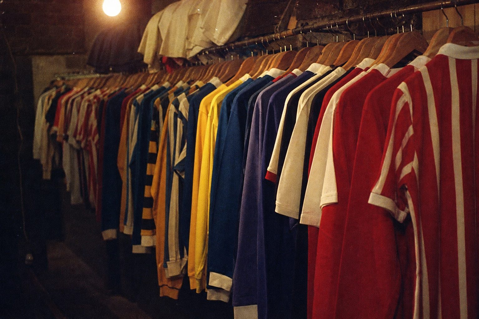 Row of vintage football shirts in different colours hanging in a dim kit room (picture made with AI)
