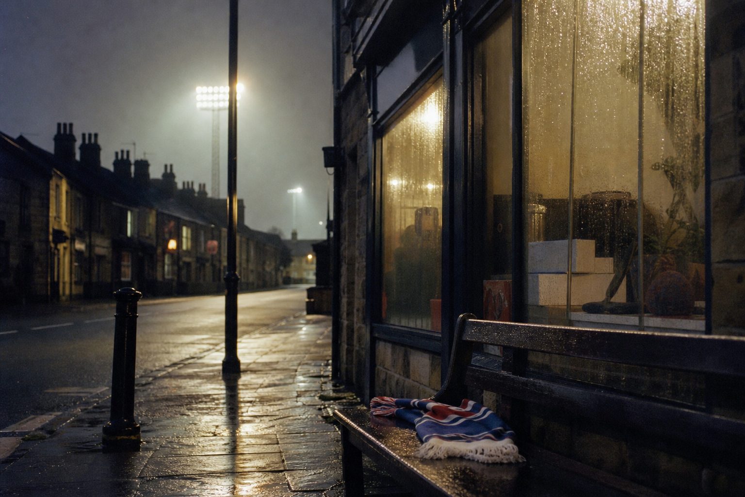 Rainy high street at dusk with a scarf on a bench and distant stadium floodlights (picture made with AI)