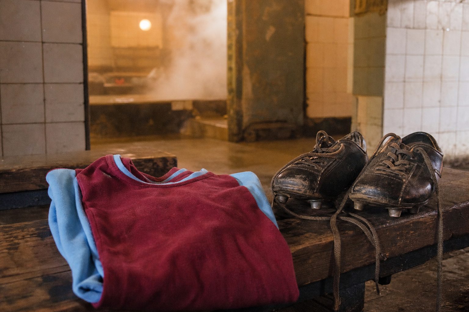 Plain claret and light blue football shirt beside muddy boots in an old dressing room (picture made with AI)