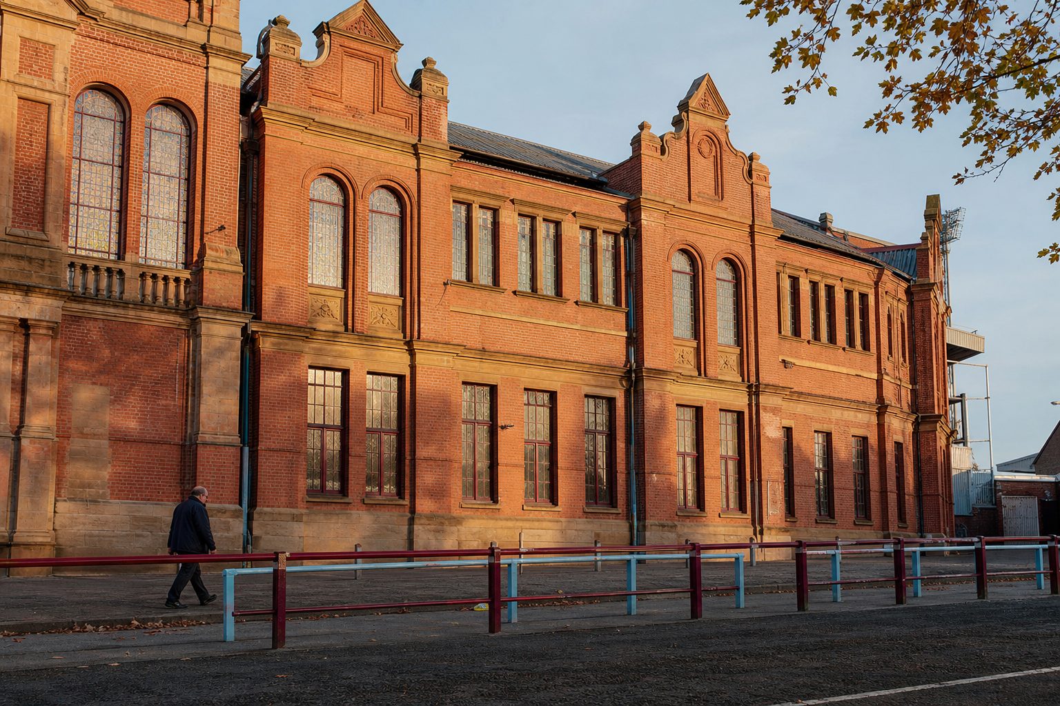 Red-brick Edwardian football stand facade with arched windows in low autumn sunlight (picture made with AI)