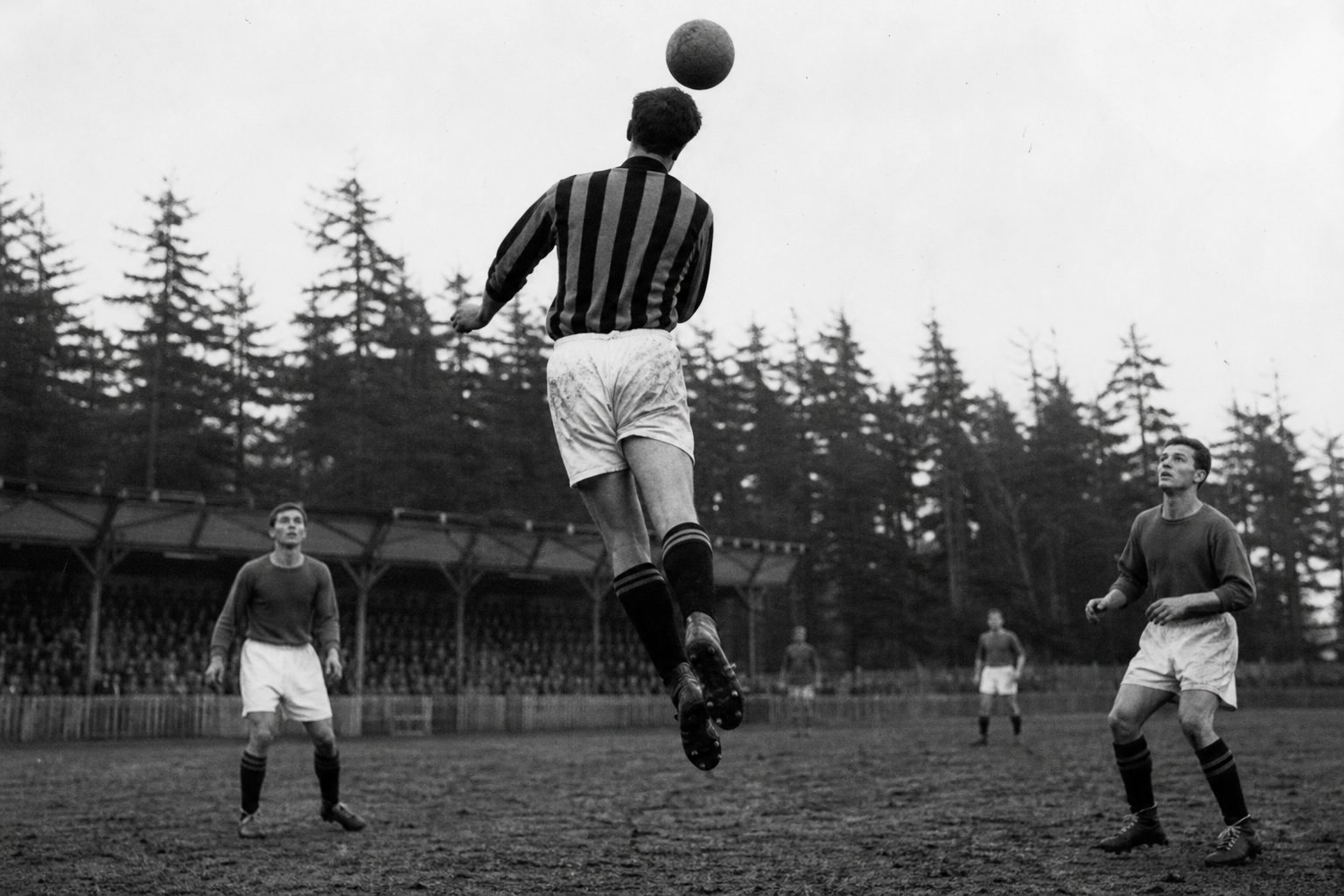 Footballer in a striped shirt leaping to head a leather ball on a muddy pitch (picture made with AI)