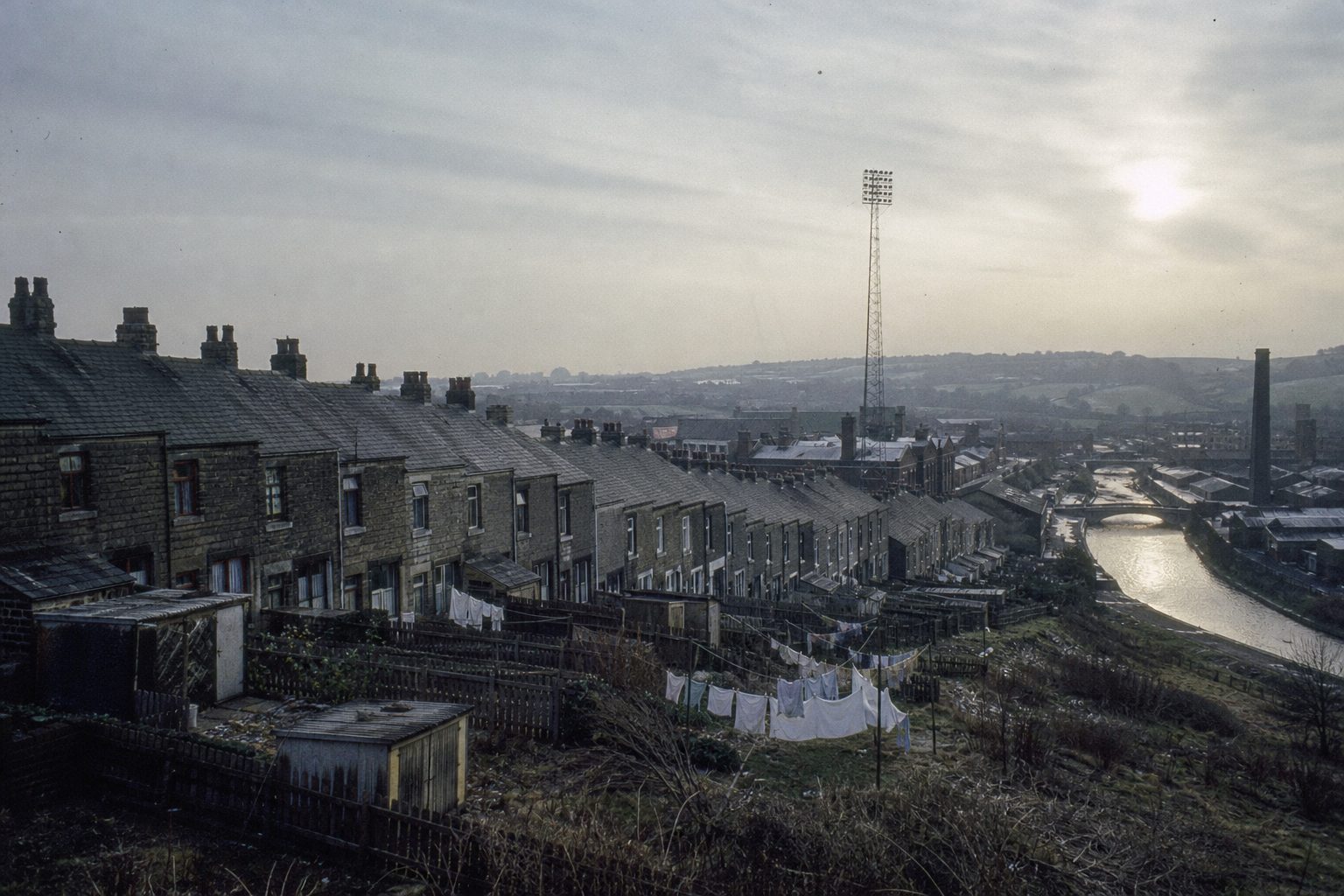Stone terraces, mill chimneys and a floodlight pylon on a Lancashire hillside (picture made with AI)