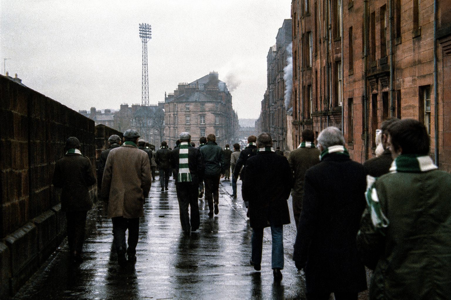 Supporters in green and white scarves walking along a sandstone tenement street (picture made with AI)