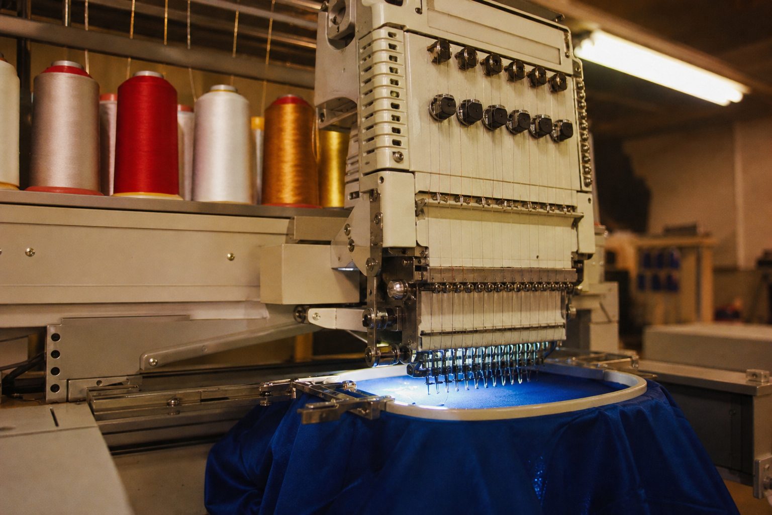 Embroidery machine stitching a royal blue shirt with spools of red, white and gold thread (picture made with AI)