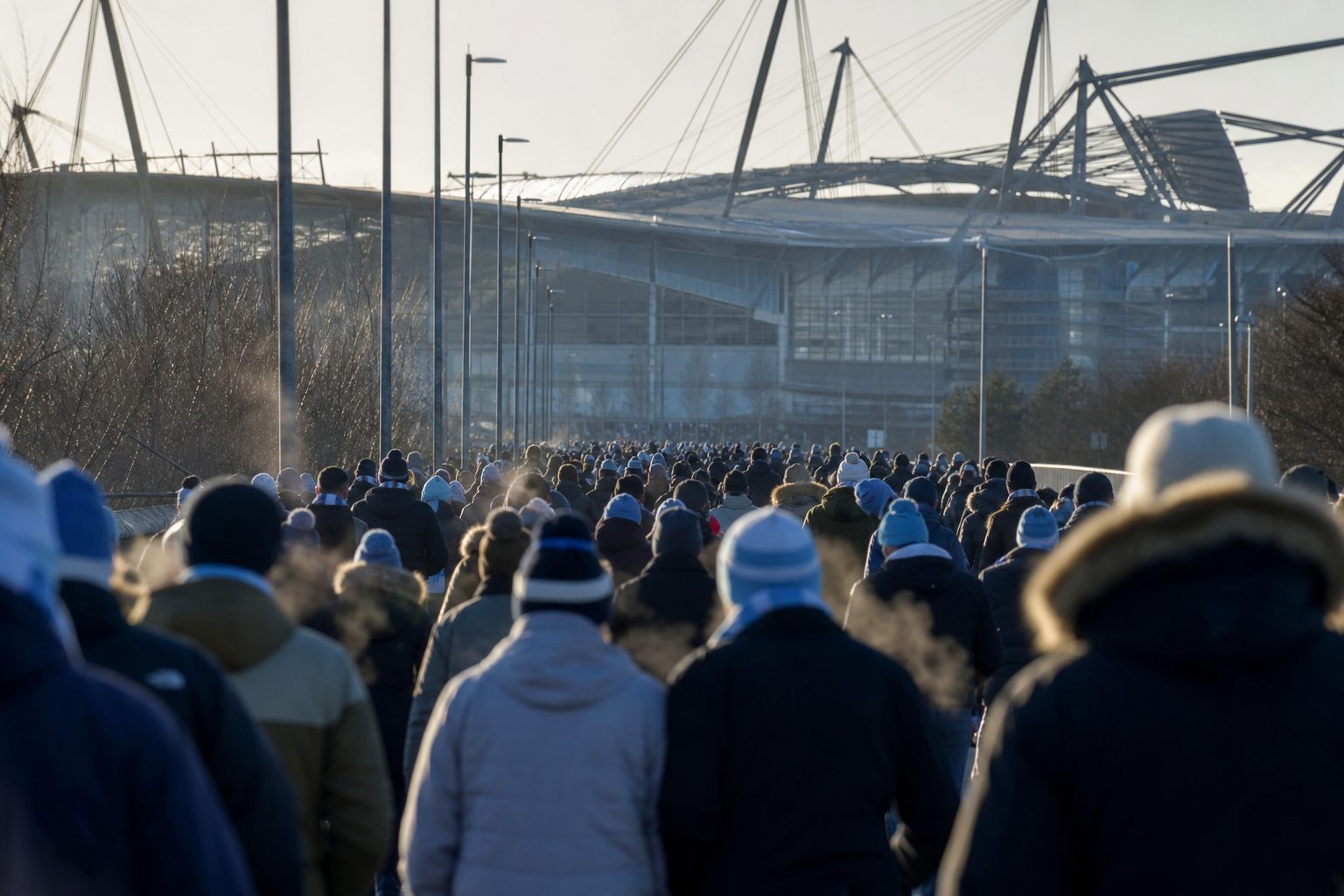 Supporters in sky-blue scarves walking towards a modern stadium on a winter afternoon (picture made with AI)