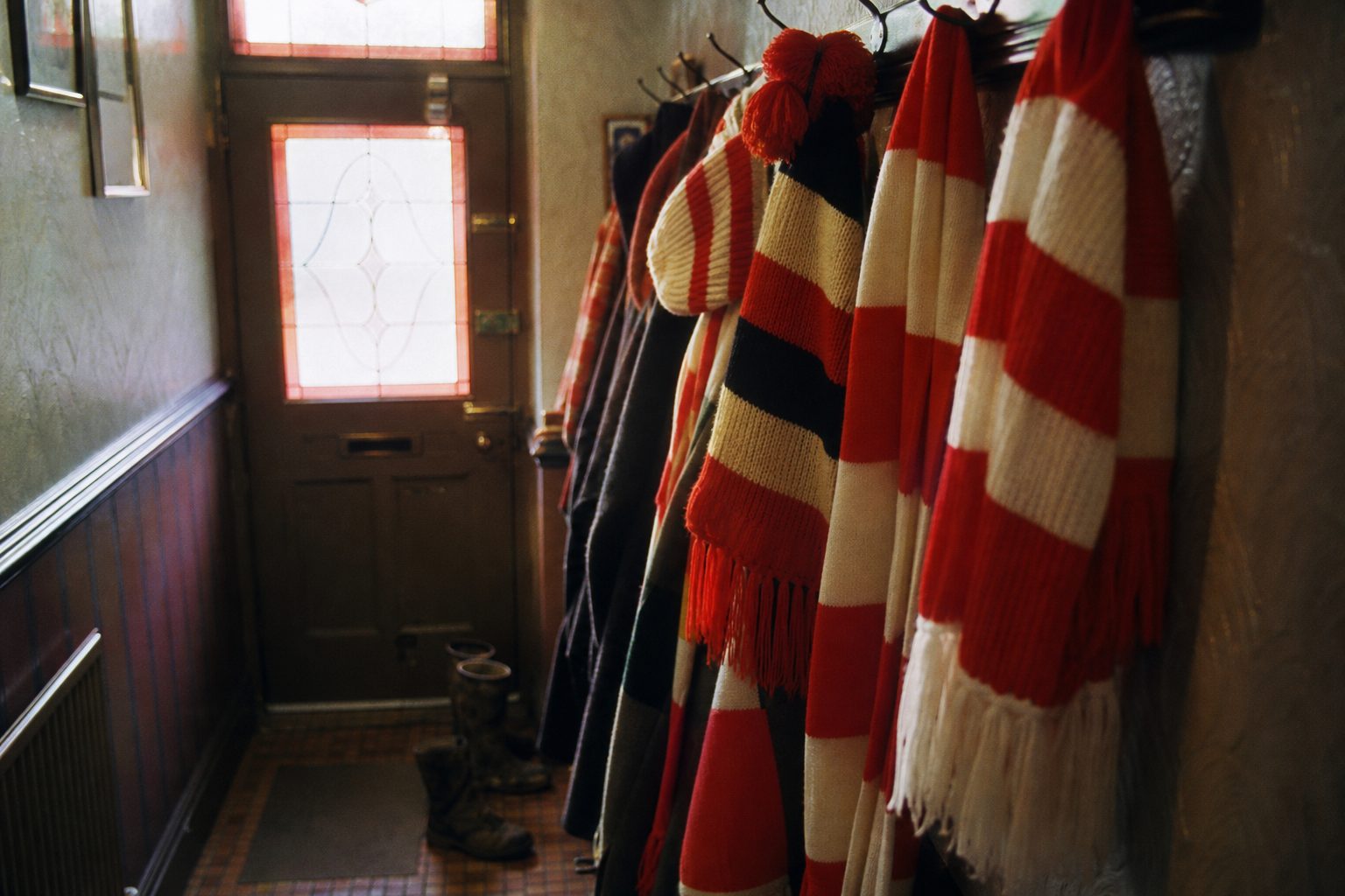 Red and white knitted scarves and hats hanging from hooks in a narrow hallway (picture made with AI)