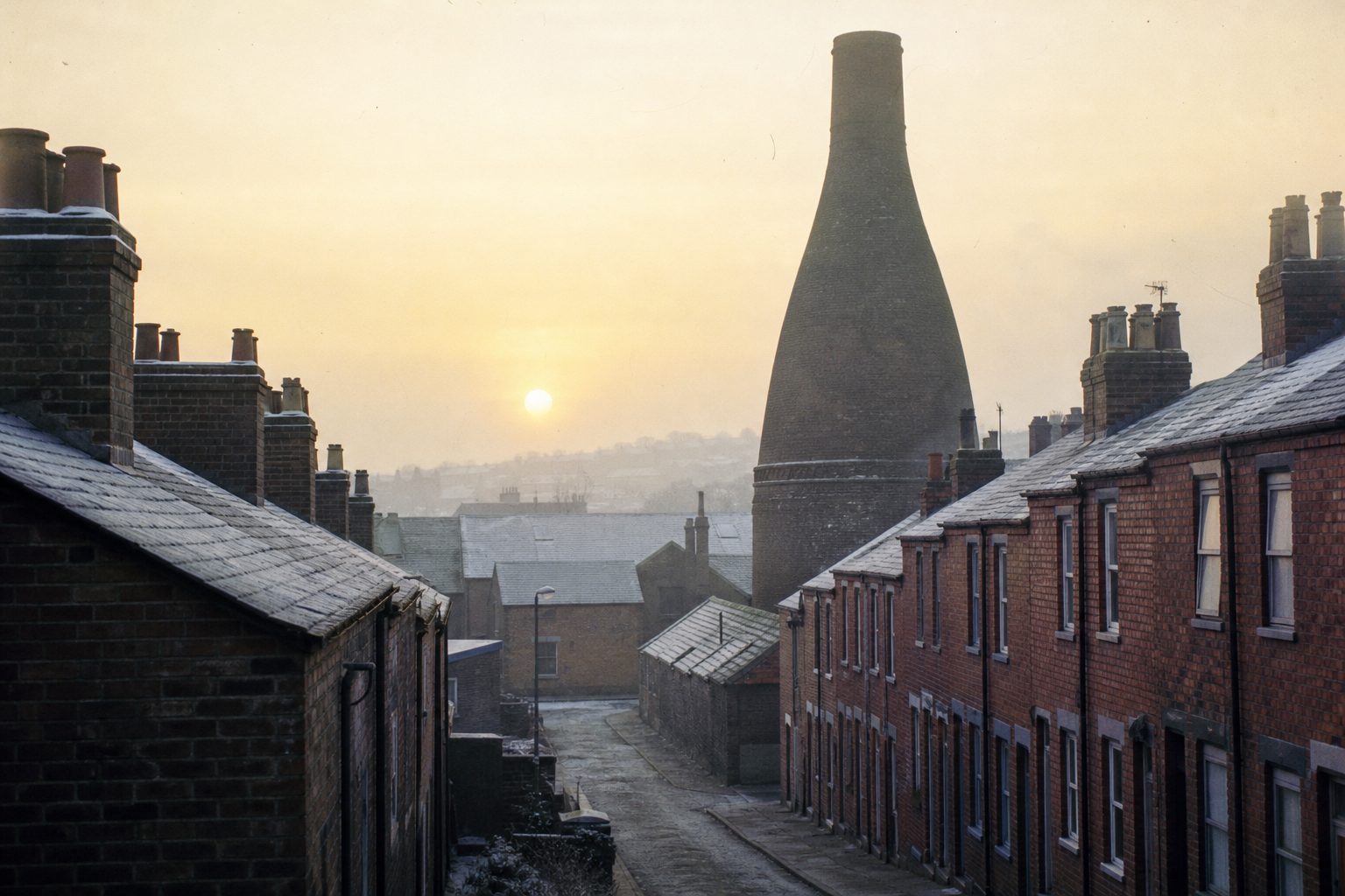 Brick bottle kiln rising above red-brick terraced houses on a misty winter morning (picture made with AI)