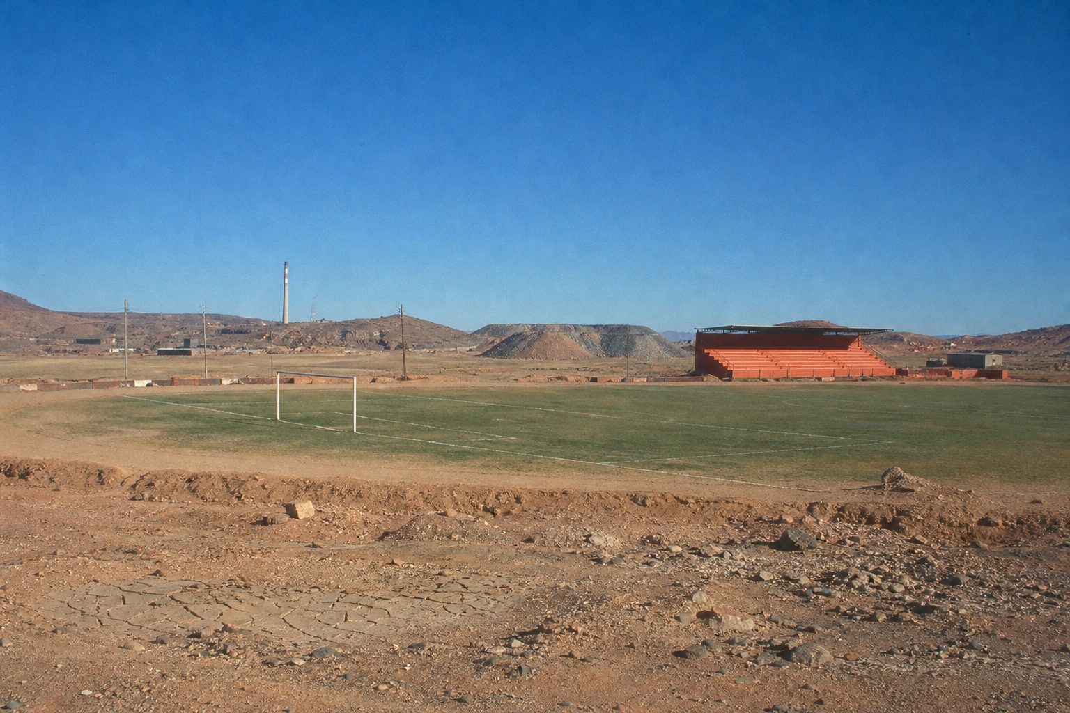 Small orange stand beside a worn pitch in a dry desert mining town (picture made with AI)