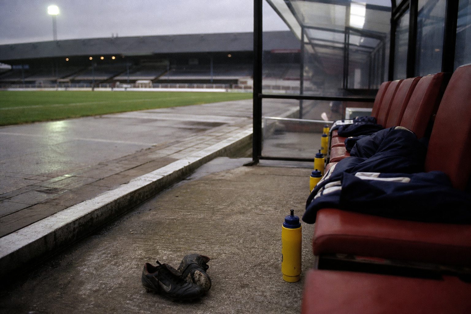 Empty substitutes' bench with folded tracksuit tops and muddy boots (picture made with AI)