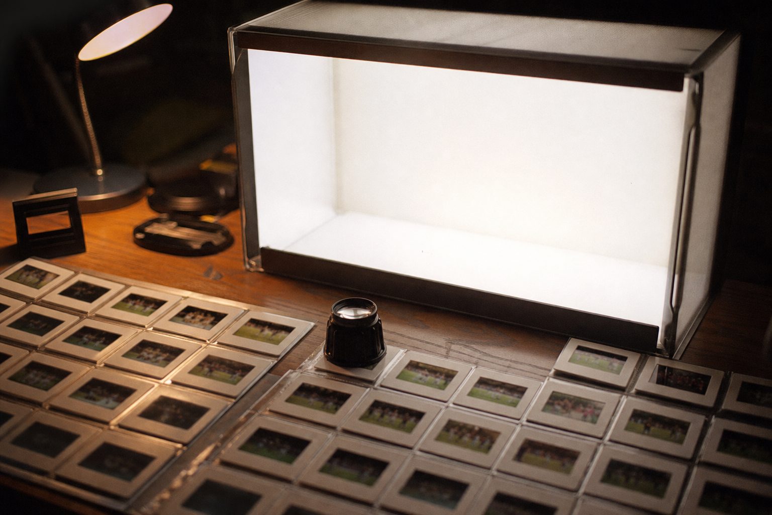 A light box covered with rows of football slide film and a magnifying loupe (picture made with AI)