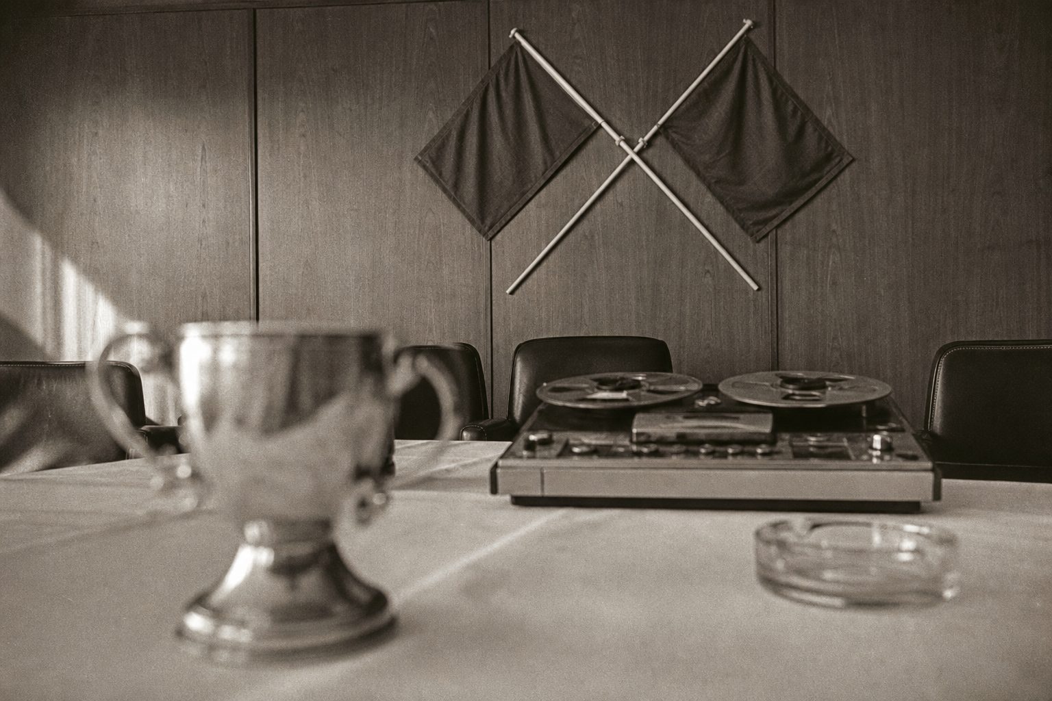 Blurred silver trophy on a boardroom table beside crossed plain pennants and a tape recorder (picture made with AI)